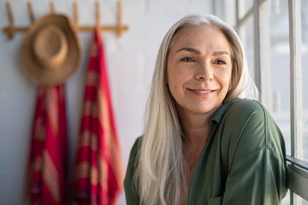 Senior stylish woman thinking Portrait of beautiful senior woman sitting near big window at home and contemplate. Closeup face of fashionable old woman at home relaxing in living room. Mature woman thinking while looking away.